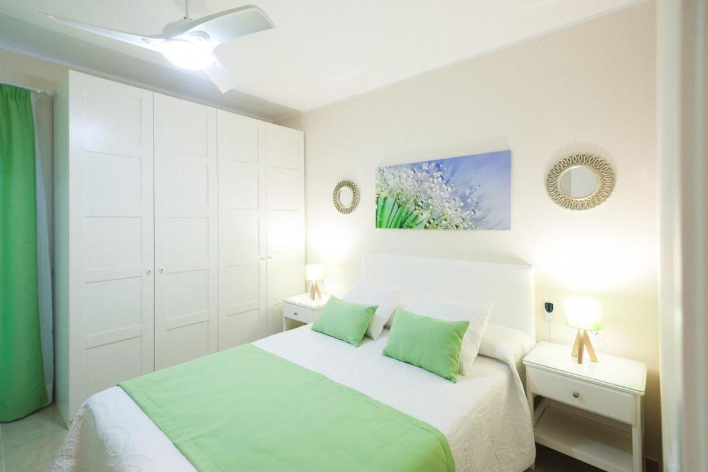 a white bedroom with a bed with green pillows at La Entallada in Las Playas