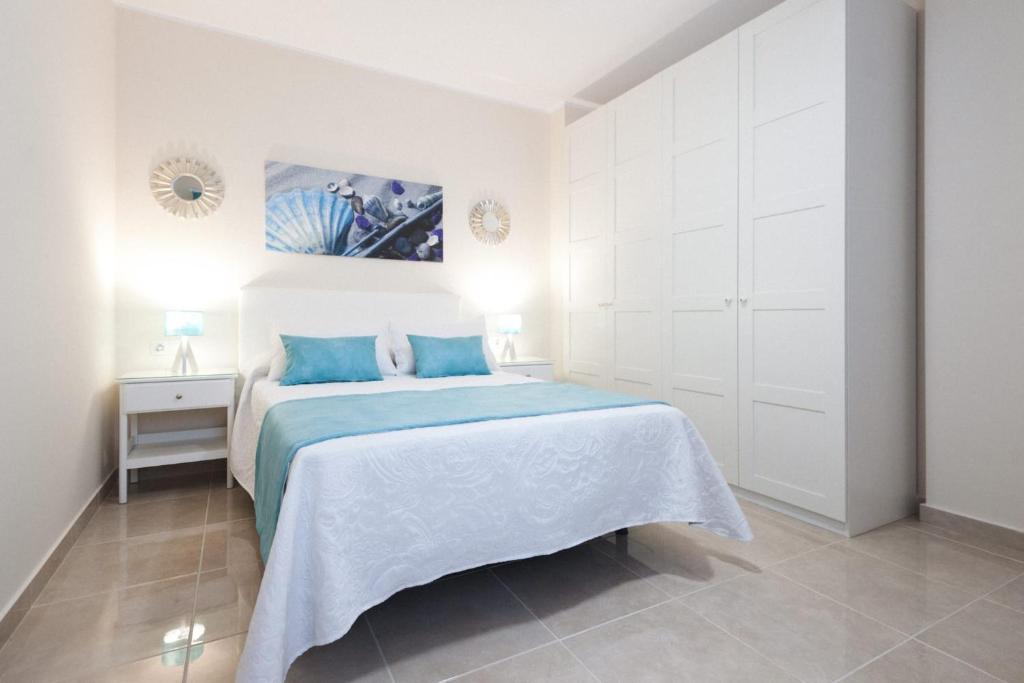 a white bedroom with a blue bed and a mirror at El faro in Las Playas