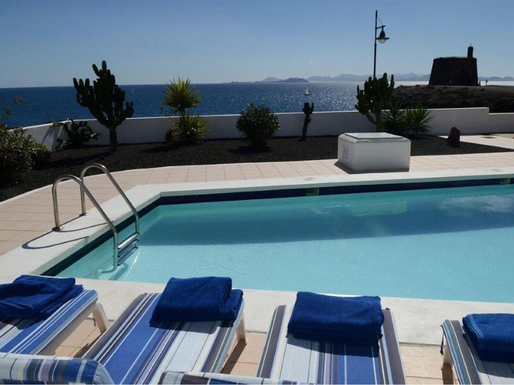 a swimming pool with two lounge chairs and the ocean at Villas Volcan - Ocean Dreams in Playa Blanca