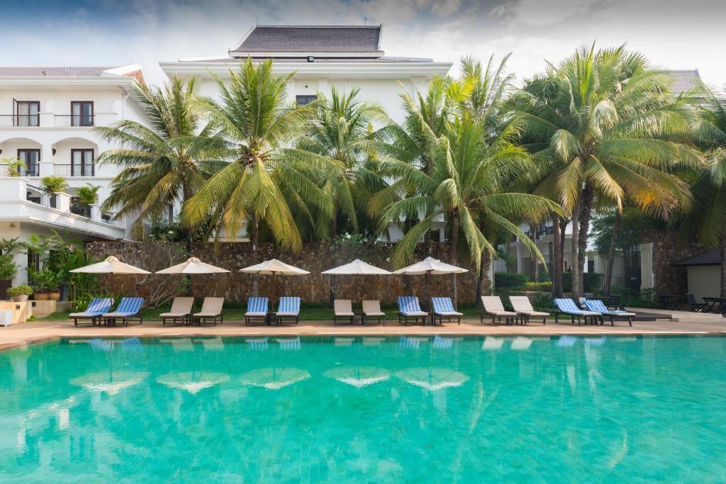 a swimming pool with chairs and palm trees and a building at Lotus Blanc Resort in Siem Reap