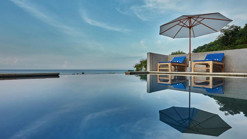 a swimming pool with two chairs and an umbrella at Villa Aska in Amed