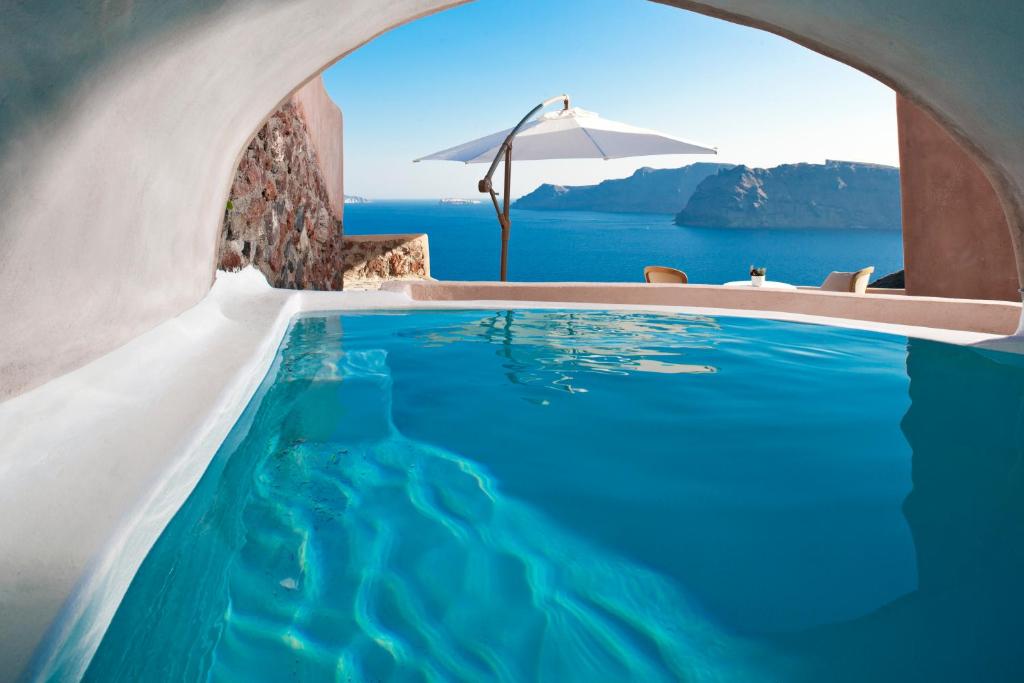 a swimming pool with an umbrella and the ocean at Armeni Luxury Villas in Oia
