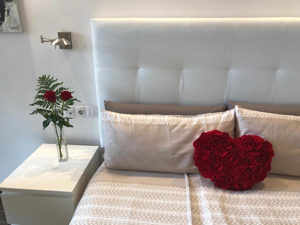 Una almohada de corazón roja en una cama con un jarrón de flores en La Perla, en Puerto de la Cruz