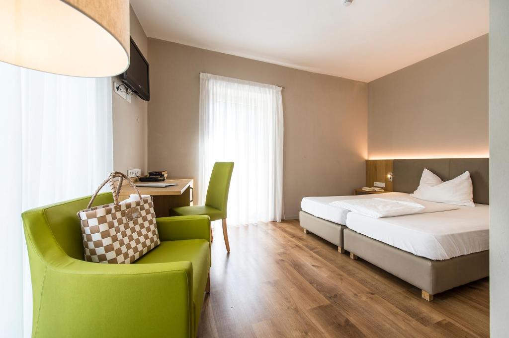 ライヴェスにあるHotel CampingPark Steinerのベッドと緑の椅子が備わるホテルルームです。