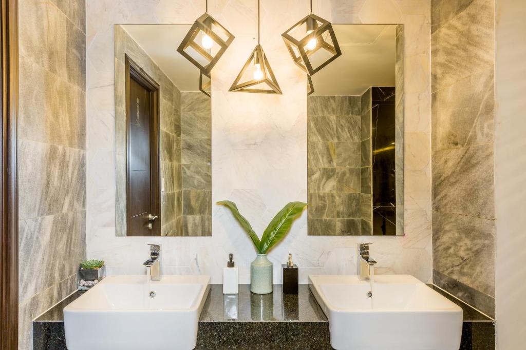 A marble-look bathroom vanity has two square basins, separate mirrors, and geometric pendant lights.