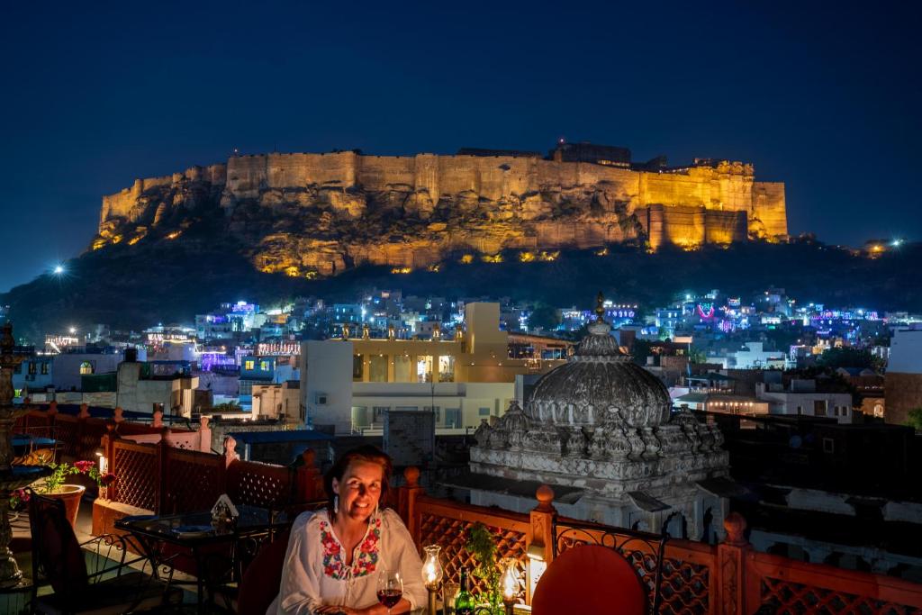 a man sitting on a balcony with a view of the acropolis at night at Haveli Inn Pal in Jodhpur