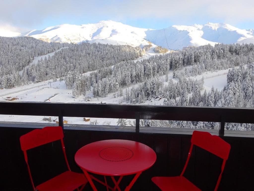 - une table et des chaises rouges sur un balcon avec des montagnes enneigées dans l'établissement BIENVENUE AU LIORAN, à Le Lioran