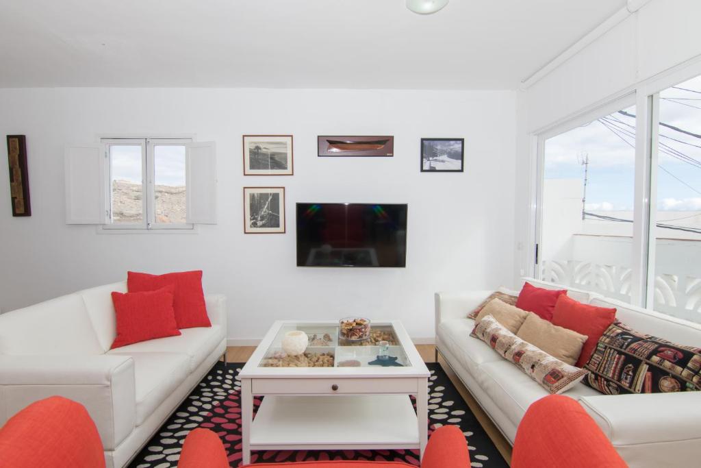 a white living room with a white couch and red pillows at HomeForGuest Apto 20 PASOS DEL MAR, EL PORIS CON VISTA MAR in Arico el Nuevo