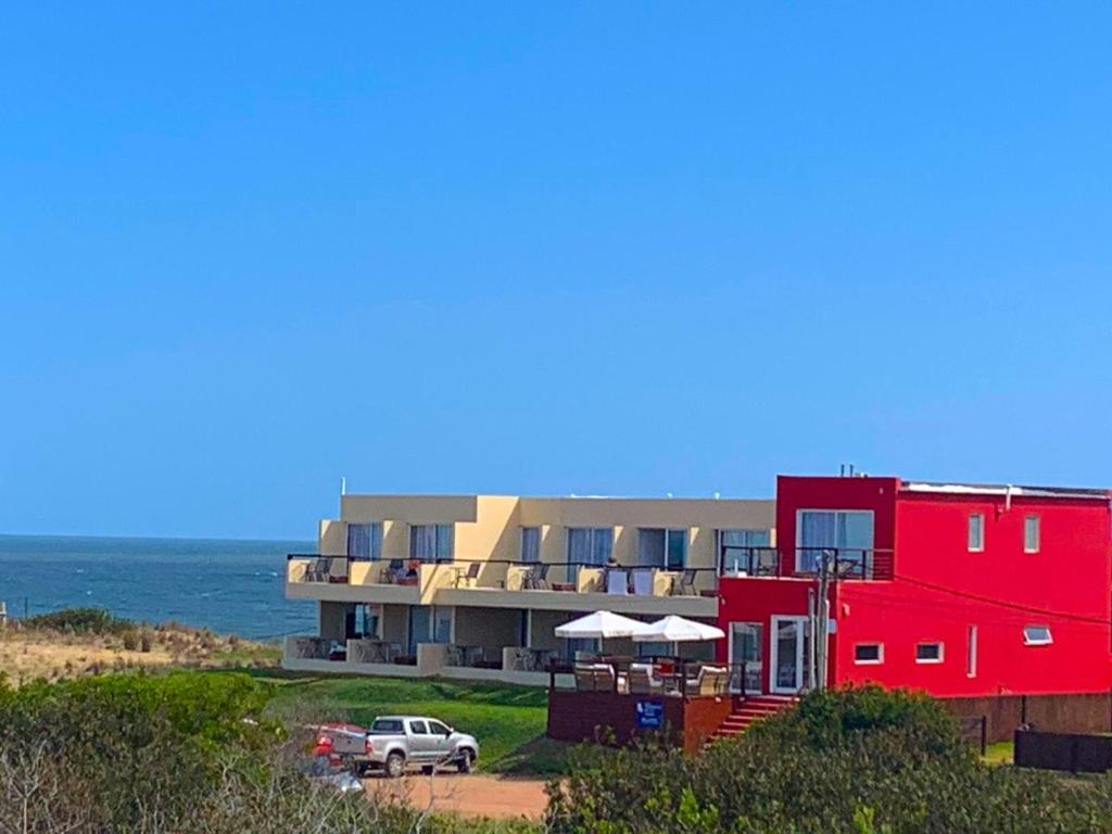 a red building on the beach next to the ocean at Terrazas de la Viuda in Punta Del Diablo