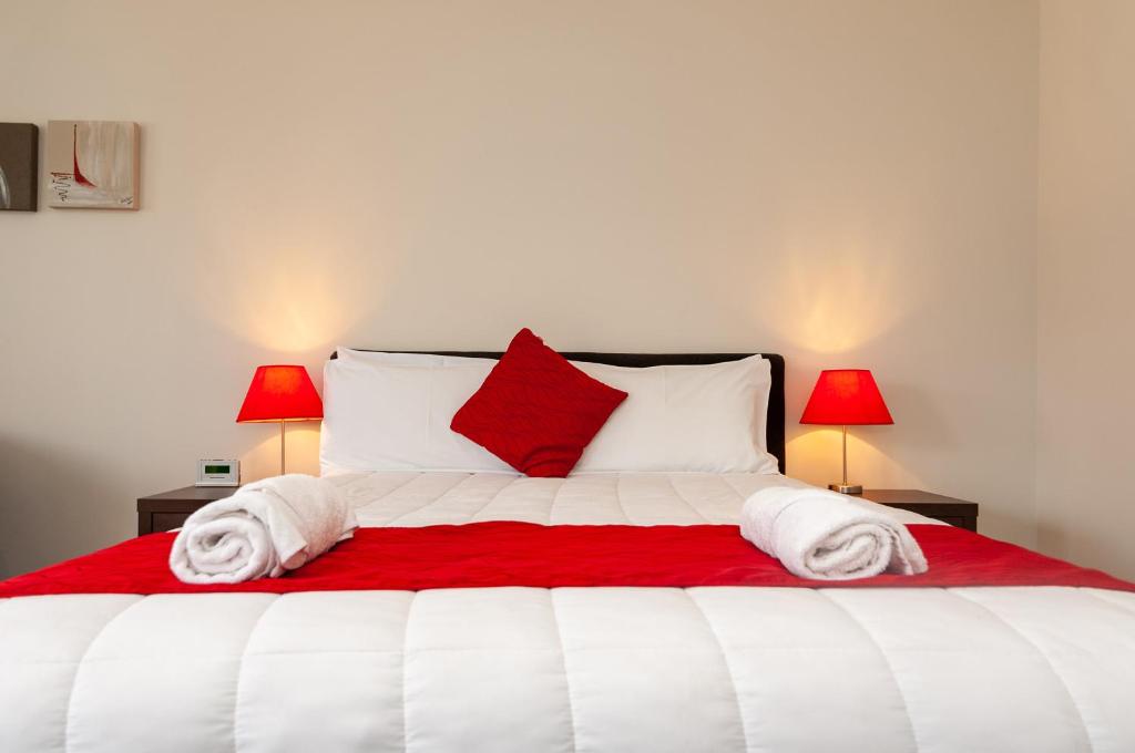 un letto bianco con cuscini rossi e 2 lampade di The Park Motel a Hawera