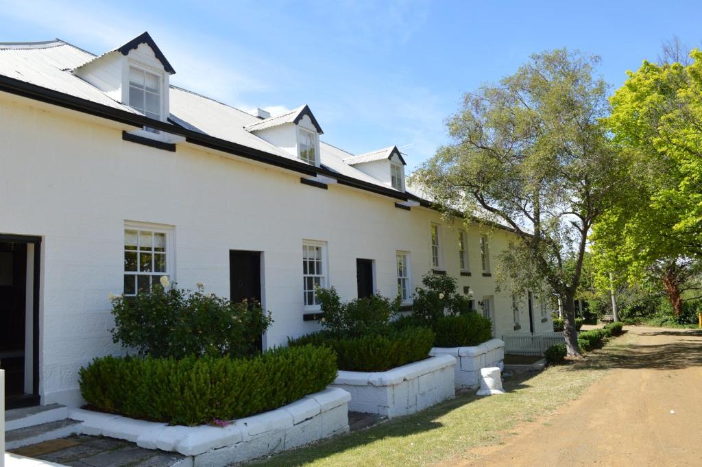 an old white house with bushes and trees at Lythgo's Row Colonial Cottages in Pontville