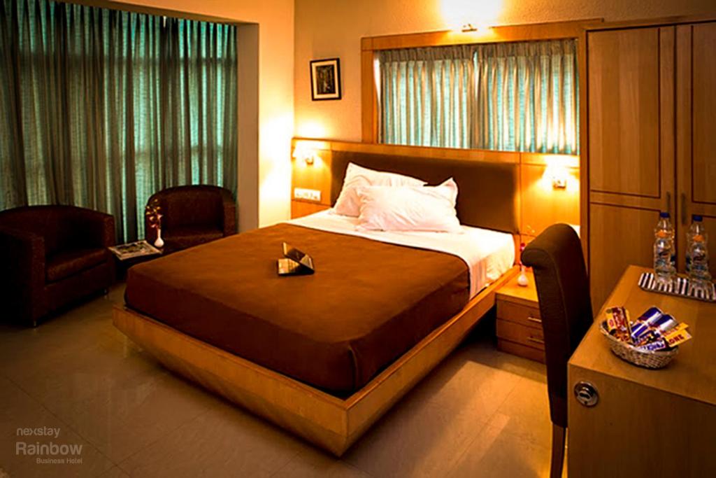 a bedroom with a large bed and a chair at New Rainbow Business Hotel in Bangalore