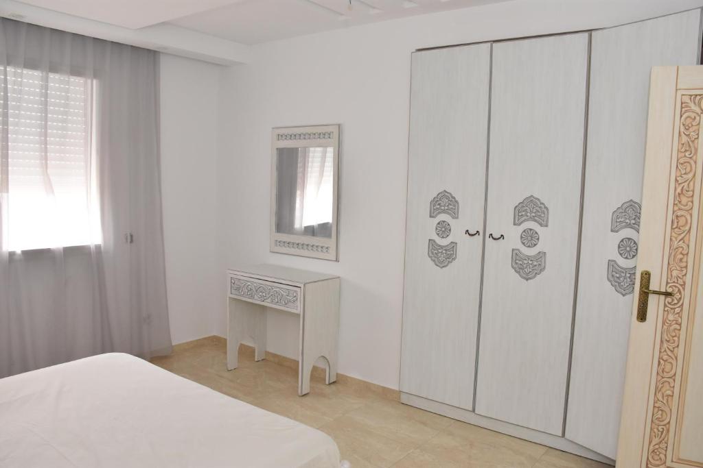 a white bedroom with a bed and a dresser at Arabesque Style - 2 appartements in Kelibia