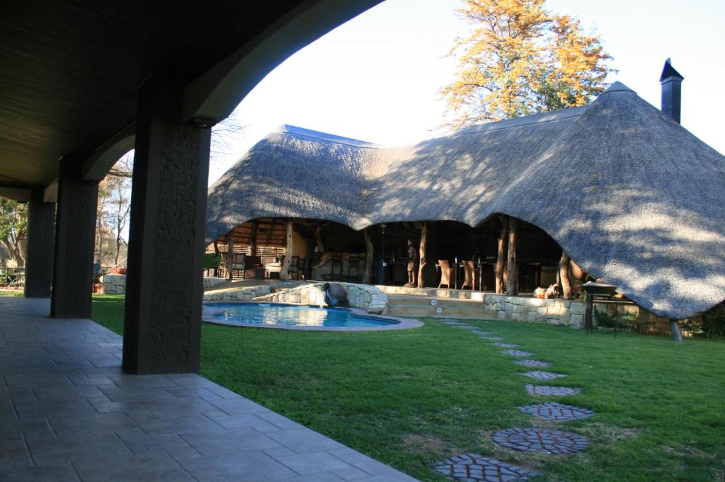 un grand bâtiment avec un toit de chaume et une piscine dans l'établissement AFRICAN DREAMS GUESTHOUSE, à Okahandja