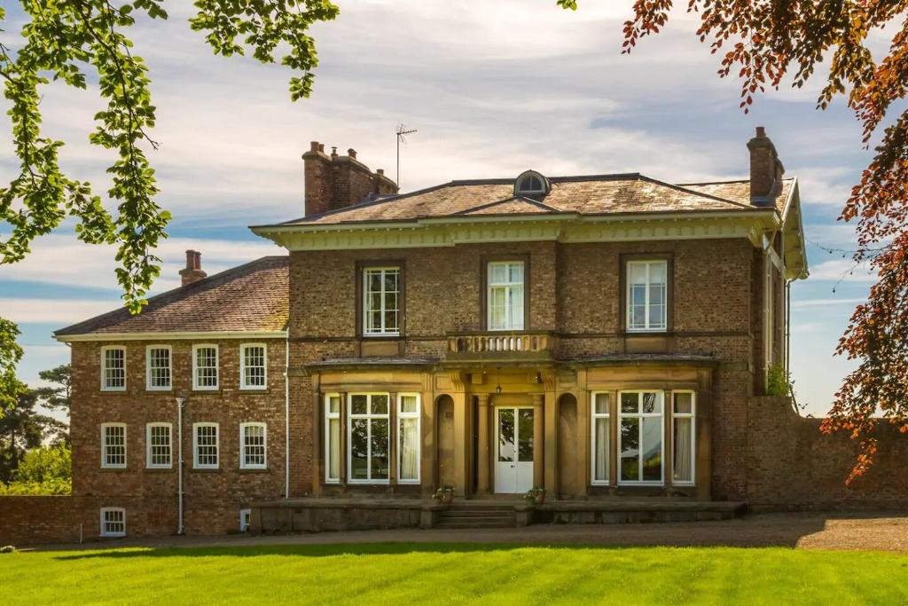 an old brick house with a lawn in front at The Wing at Brook Hall in Tadcaster