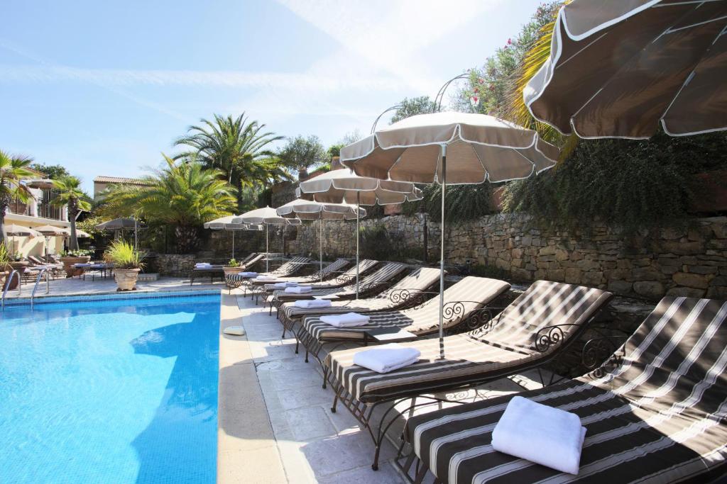 a row of lounge chairs with umbrellas next to a swimming pool at La Bastide de Valbonne in Valbonne