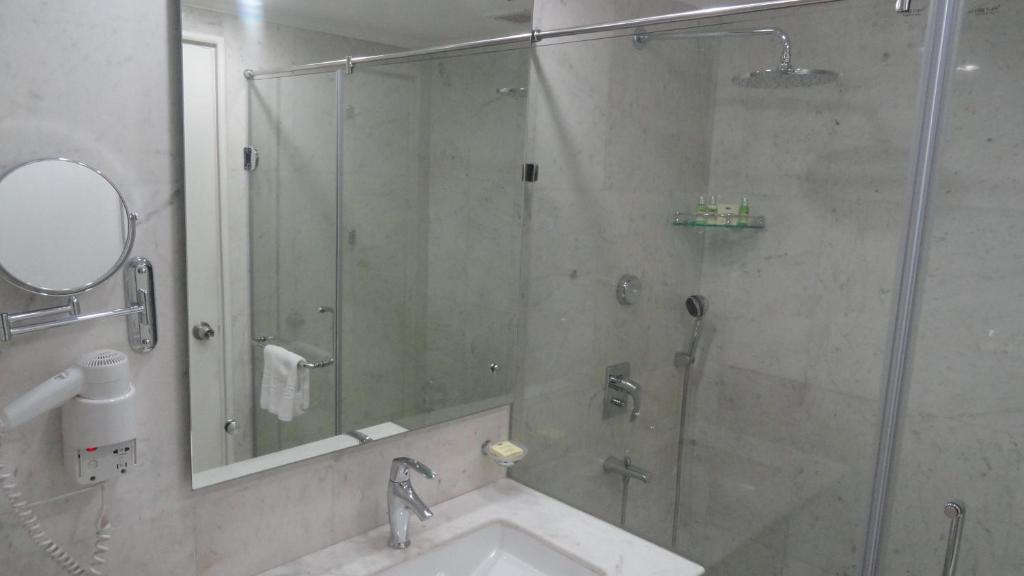 a bathroom with a shower with a sink and a glass shower door at Hotel Clarks Shiraz in Agra