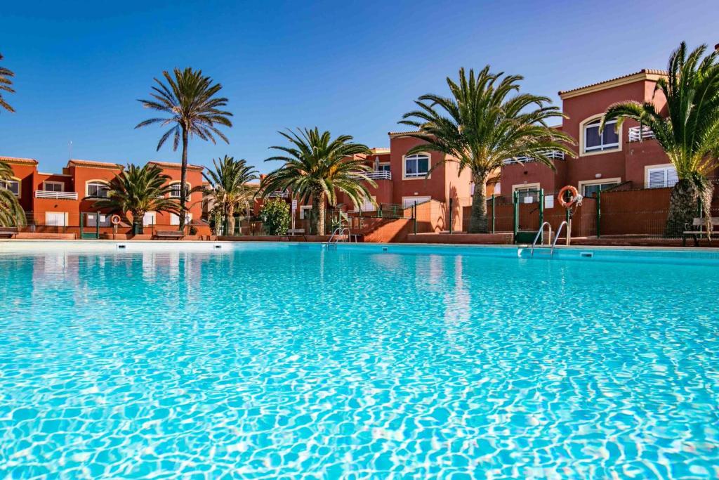 une grande piscine avec des palmiers et des bâtiments dans l'établissement Home FTV, by Comfortable Luxury, à Corralejo