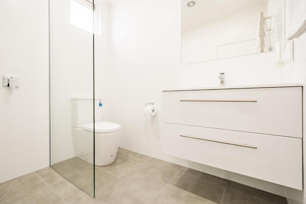 a white bathroom with a toilet and a glass shower at Argosy Motor Inn in Devonport