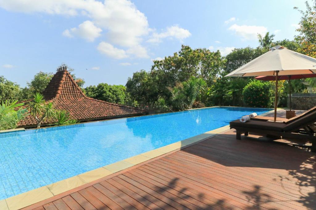 a swimming pool with a chair and an umbrella at The Sanyas Retreat in Tabanan