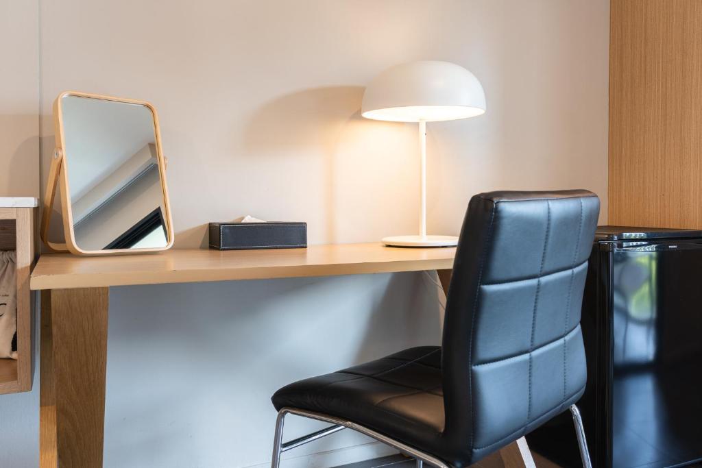 A compact built-in desk with a padded chair, lamp and tabletop mirror.