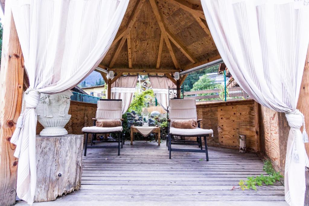 eine Markise mit Stühlen und Vorhängen auf einer Holzterrasse in der Unterkunft Gästehaus Waldrand Garni in Wiesing