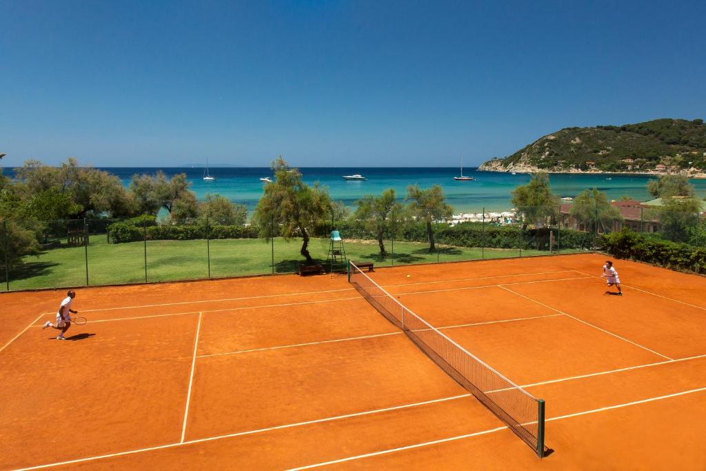 two people playing a game of tennis on a tennis court at Hotel Biodola in Portoferraio