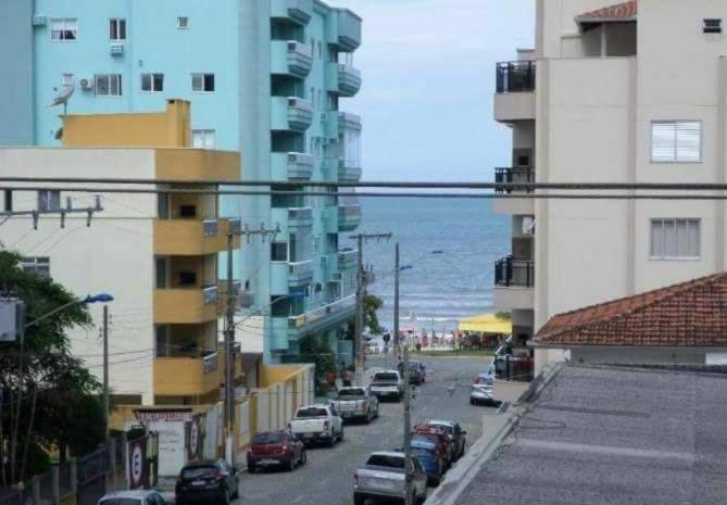 a street with cars parked next to buildings and the ocean at Meu verao em ITAPEMA in Itapema