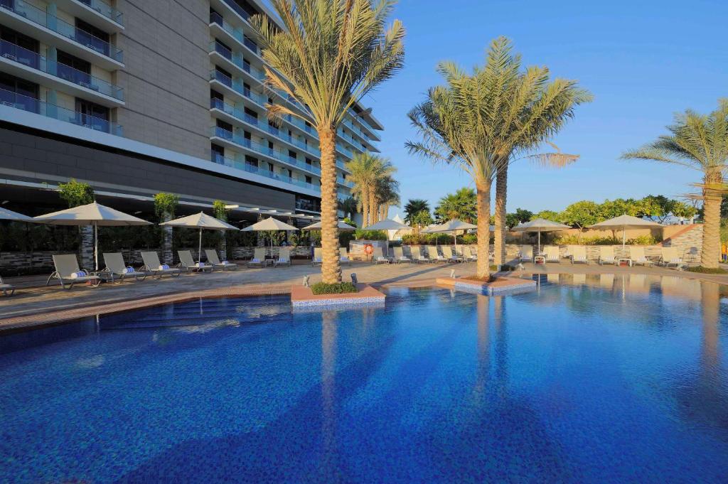 a large swimming pool with palm trees and umbrellas at Park Inn by Radisson Abu Dhabi Yas Island in Abu Dhabi