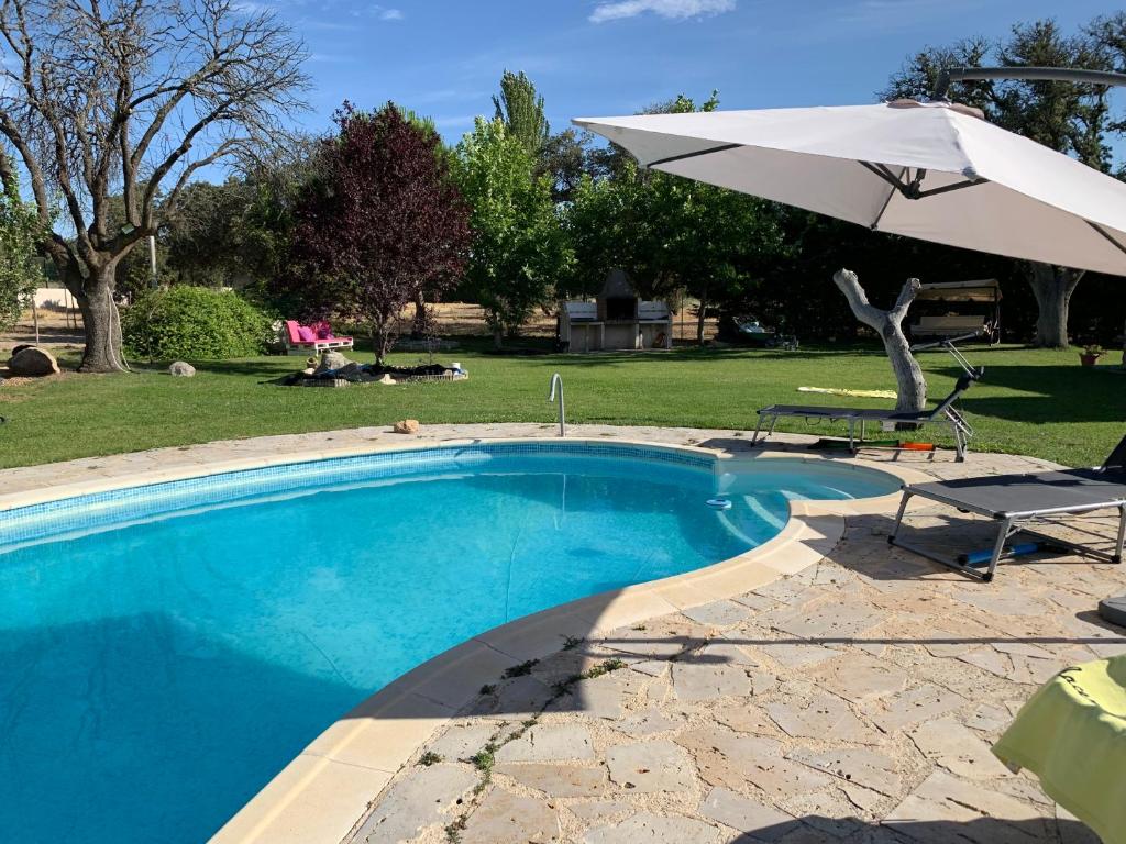 einen Pool mit einem Sonnenschirm, einem Tisch und einem Stuhl in der Unterkunft Villa Pancorbo in Velayos