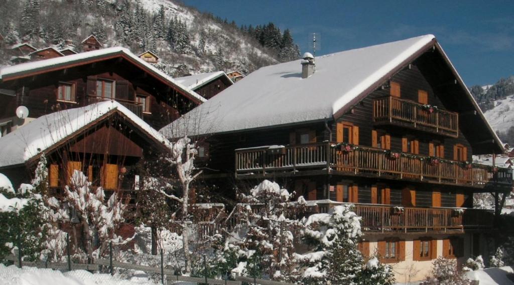 un grand bâtiment en bois avec de la neige sur le toit dans l'établissement "CHALET LES ARAVIS" chalet et Appartements, au Grand-Bornand