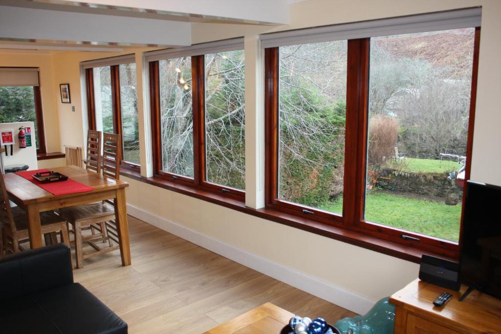 a living room with large windows and a table at Loch Ness Balcony Apartment in Drumnadrochit
