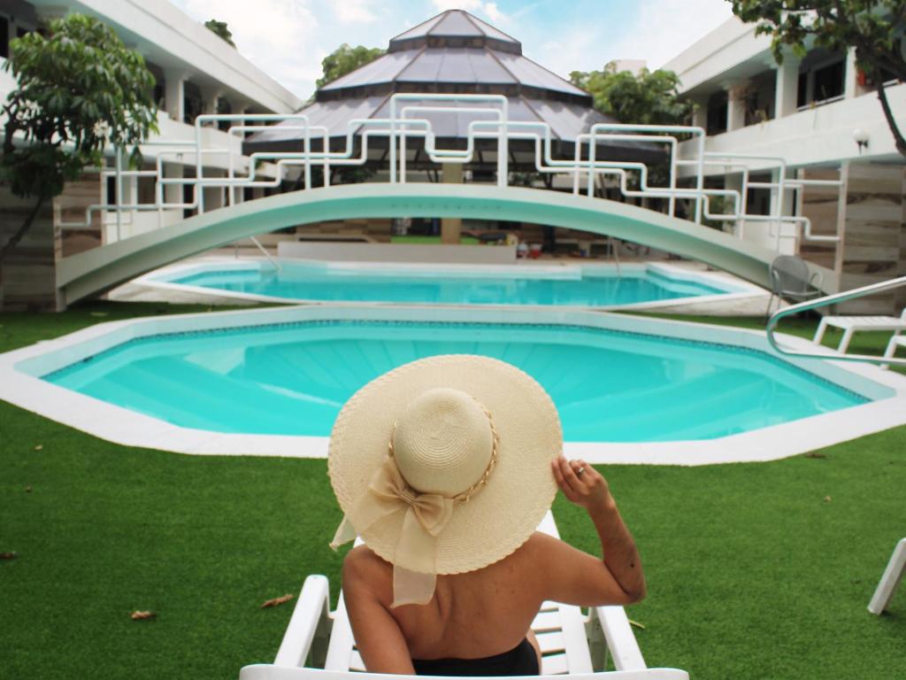 Sunio City في تيخوانا: امرأة ترتدي قبعة من القش تجلس على كرسي بجانب حمام السباحة