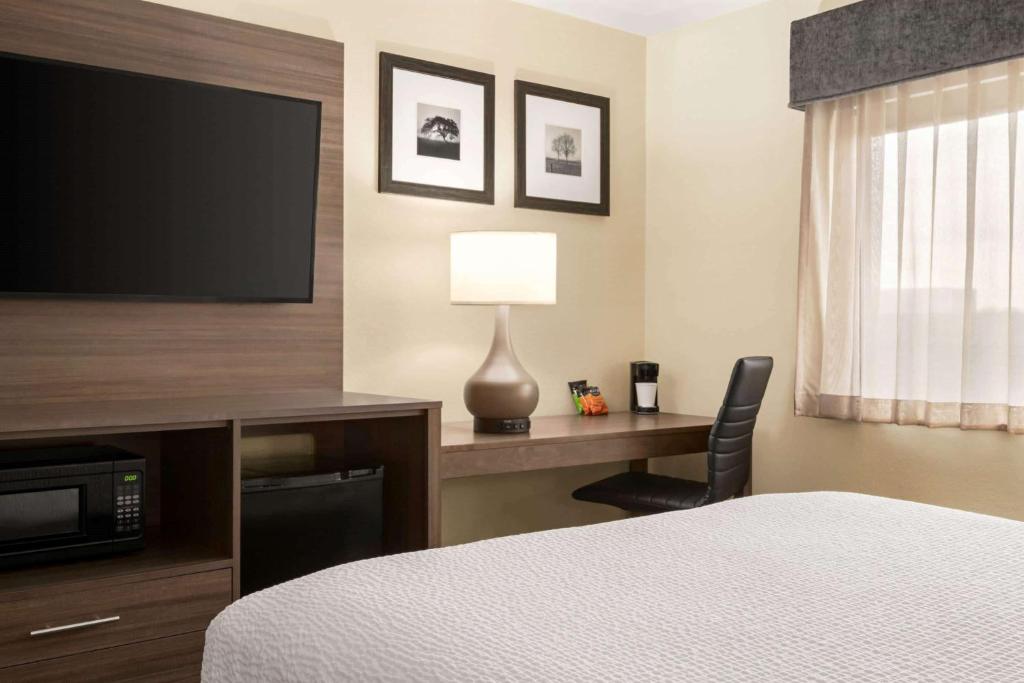 a hotel room with a bed and a desk with a television at Wingate by Wyndham Appleton in Appleton