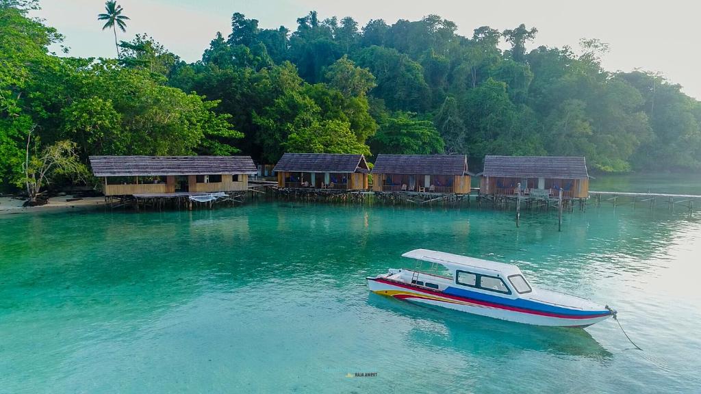 un barco en el agua junto a un grupo de casas en Hamueco Dive Resort Raja Ampat en Rabia