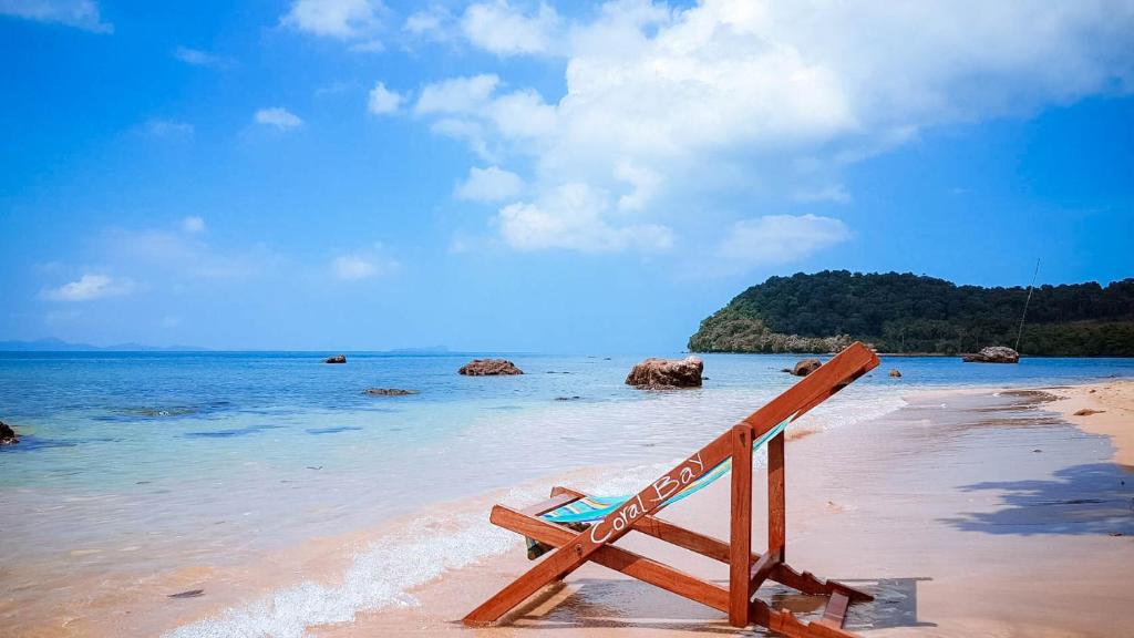 ジュム島にあるKoh Jum Coral Bay Resortの水辺の浜辺に座る木製ベンチ
