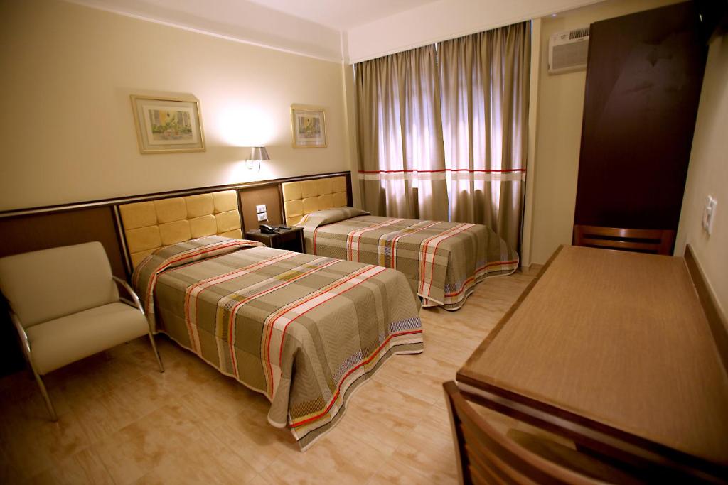 a hotel room with two beds and a chair at Soneca Plaza Hotel in Sao Paulo
