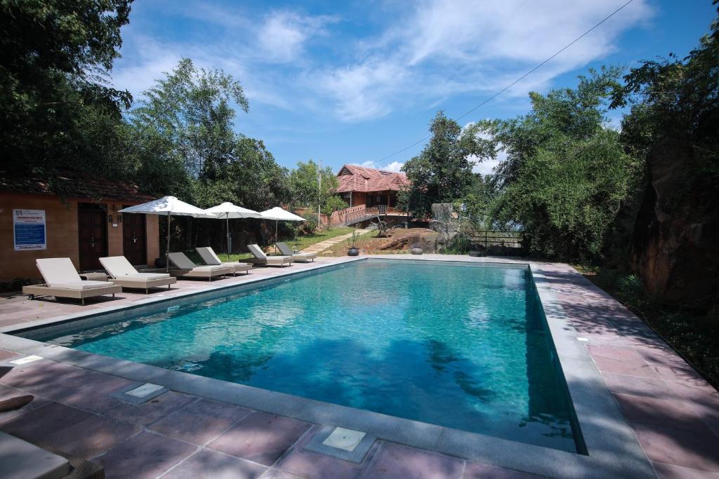 a swimming pool with chairs and umbrellas next to a house at AMARA AYURVEDA RETREAT- Overlooking Evergreen Western Ghats an ecologically sustainable living space in Kovalam in Kovalam