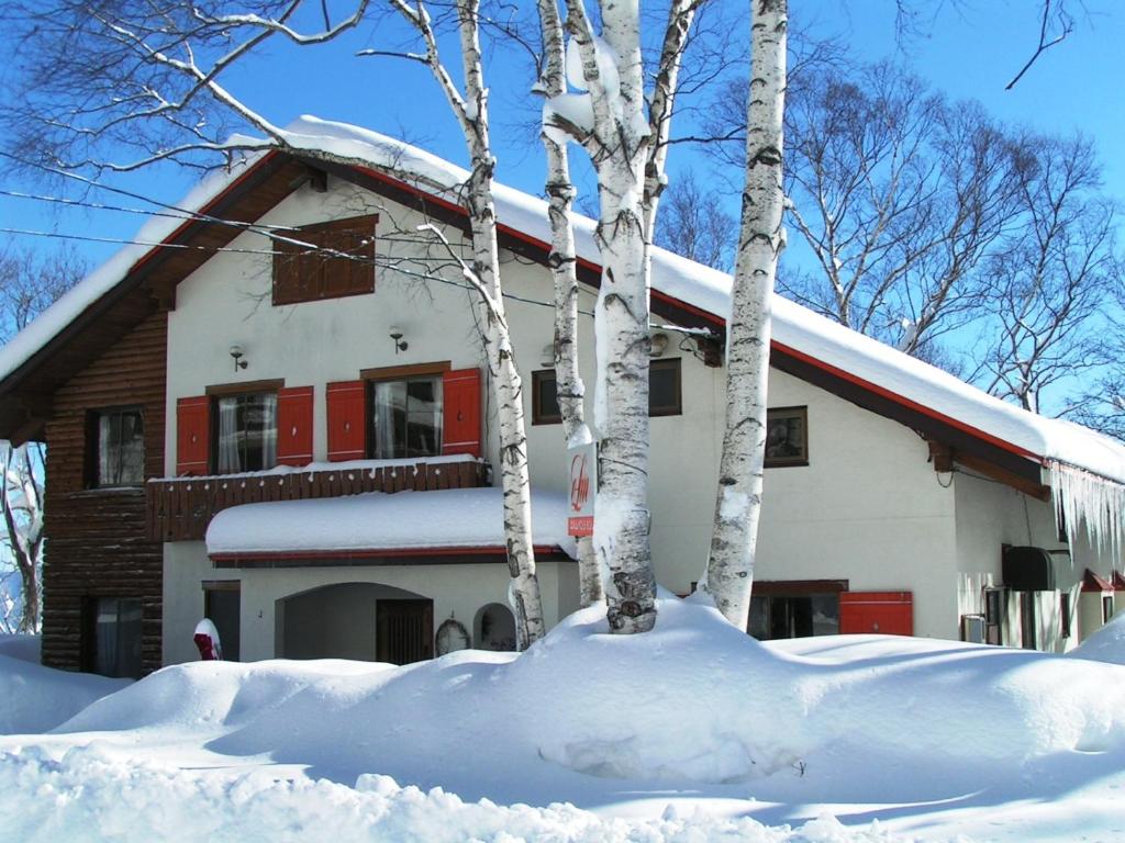 une maison recouverte de neige avec des arbres devant elle dans l'établissement Madarao Elm Pension, à Iiyama