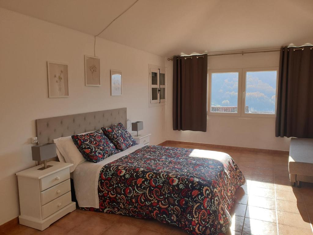 a bedroom with a bed and a nightstand and two windows at Portales de Pizarro in Béjar