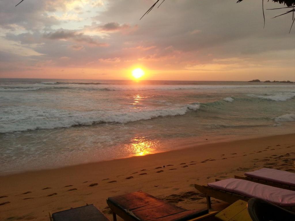 una puesta de sol en la playa con sillas y el océano en Main Reef Guest House en Hikkaduwa