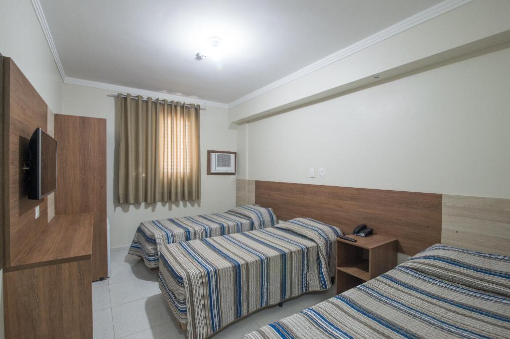 a hotel room with two beds and a television at Hotel Guarumar in Guarujá