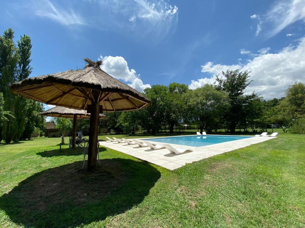 a pool with an umbrella and lounge chairs next to it at Complejo Alchucus in Villa Las Rosas