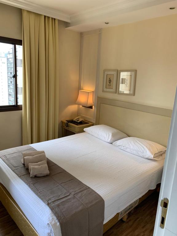 - une chambre avec un grand lit blanc et une fenêtre dans l'établissement Charmoso Flat na Vila Oimpia, à São Paulo