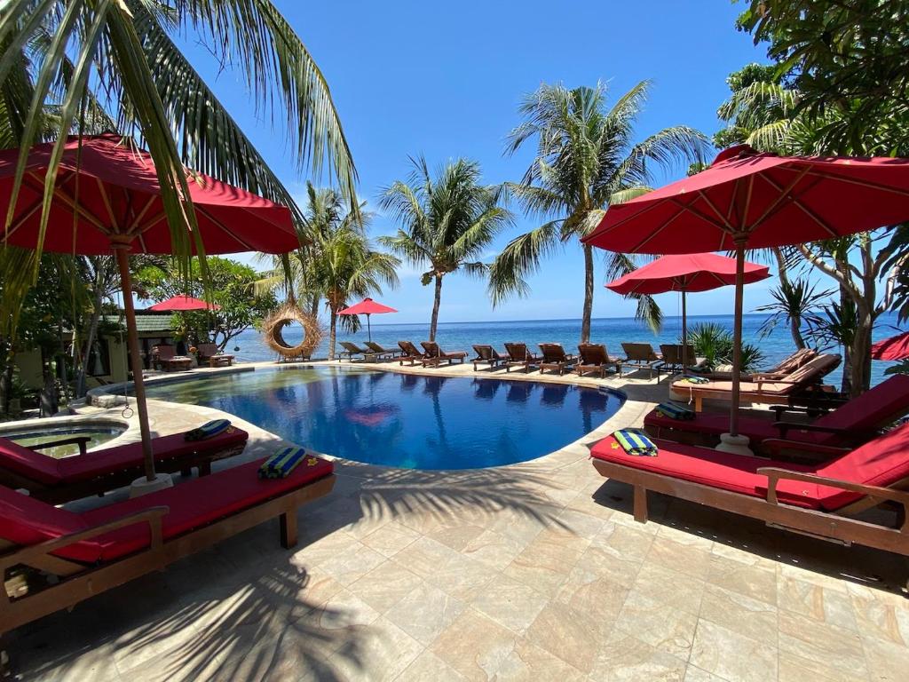 - une piscine avec chaises longues et parasols et l'océan dans l'établissement Puri Wirata Dive Resort and Spa Amed, à Amed