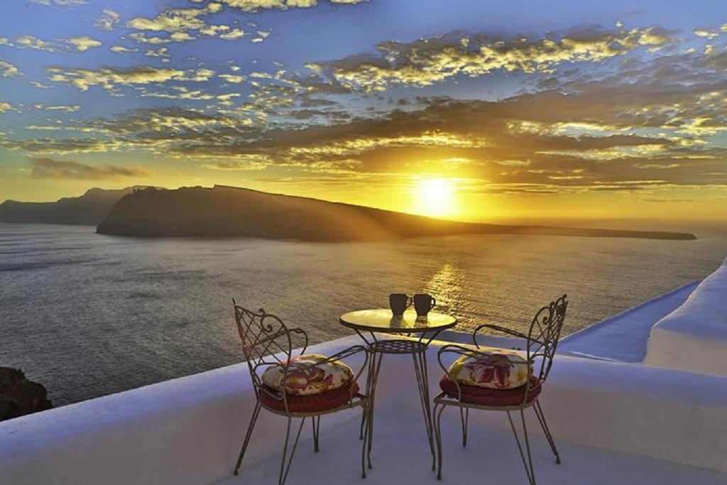 a table and chairs with a sunset over the ocean at The Architect's Cave House in Oia