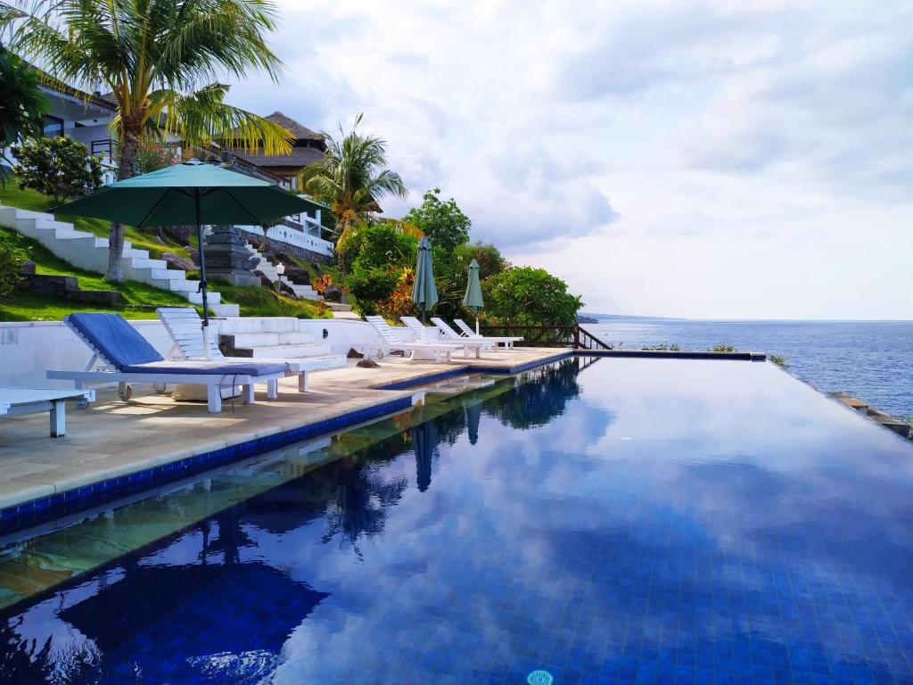 una piscina con sillas, una sombrilla y el océano en Villa Infinite Horizon, en Amed