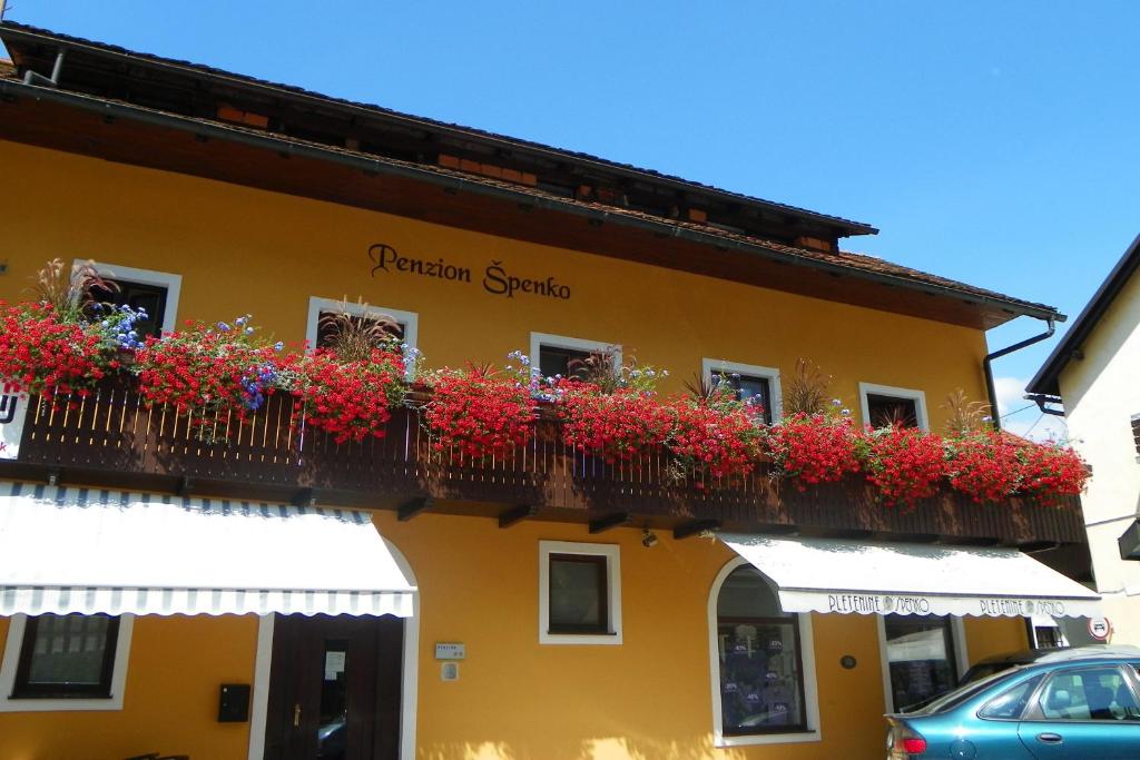 een geel gebouw met rode bloemen op een balkon bij Guesthouse Špenko in Kamnik