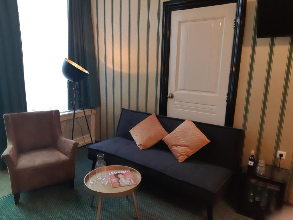 a living room with a blue couch and a chair at Hotel Johannes Vermeer Delft in Delft
