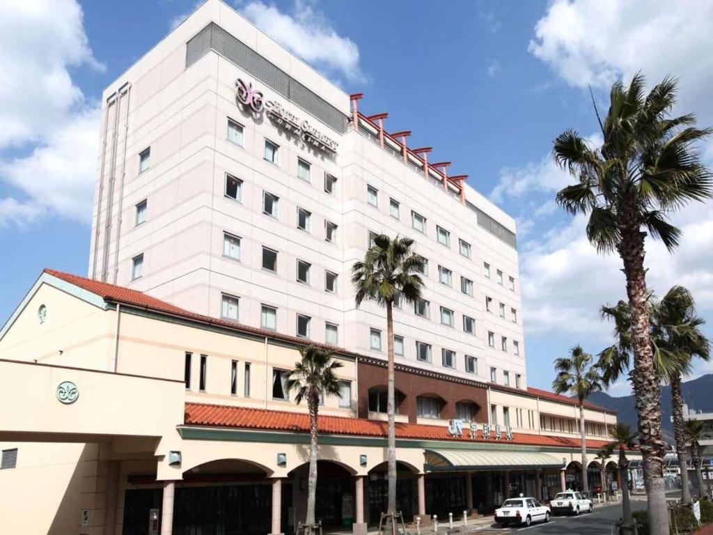 a white building with palm trees in front of it at JR Hotel Clement Uwajima in Uwajima